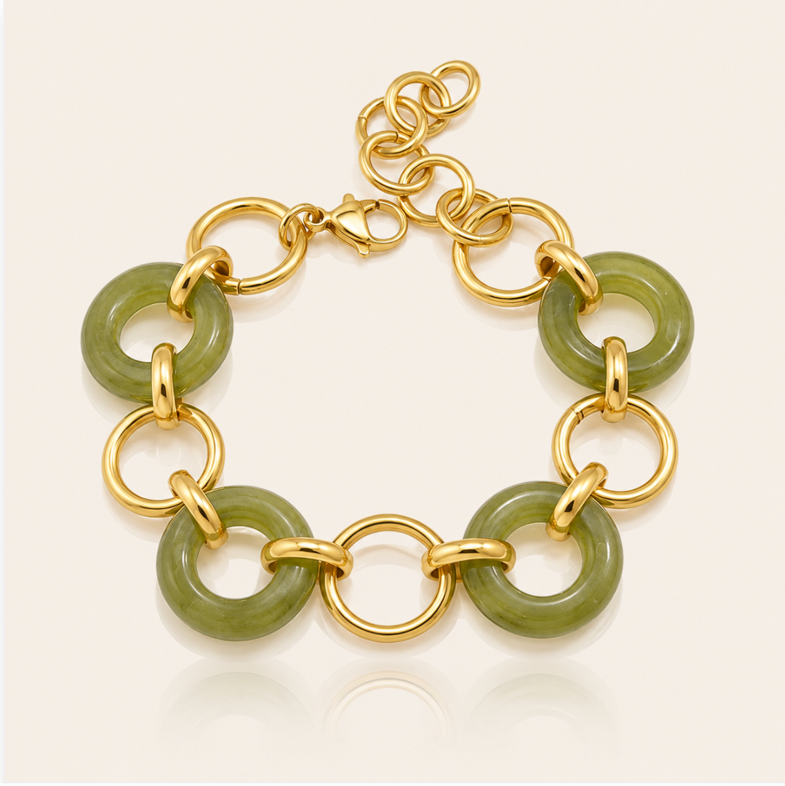 A gold chain bracelet featuring polished green jade-like disc links, displayed on a clean off-white background with a soft reflection.