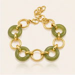 A gold chain bracelet featuring polished green jade-like disc links, displayed on a clean off-white background with a soft reflection.
