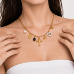 Seraphina Charms Necklace with gold paperclip chain, cross pendant, pearl, hamsa, evil eye, cherub, black bead, and marbled heart charms